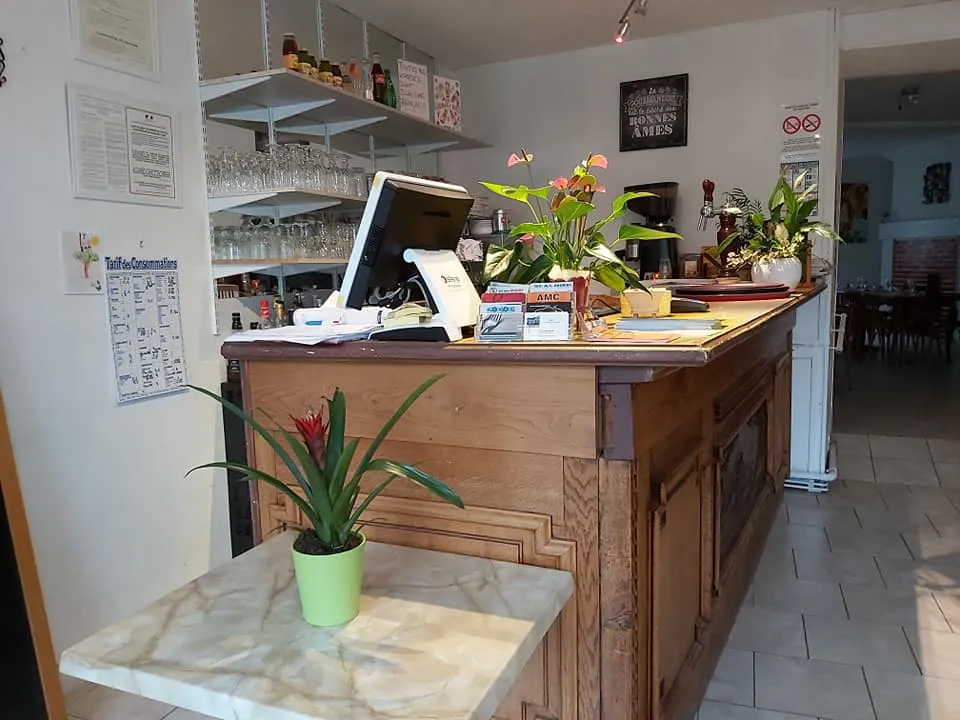 Comptoir d’accueil en bois du restaurant, entouré de plantes et de verres