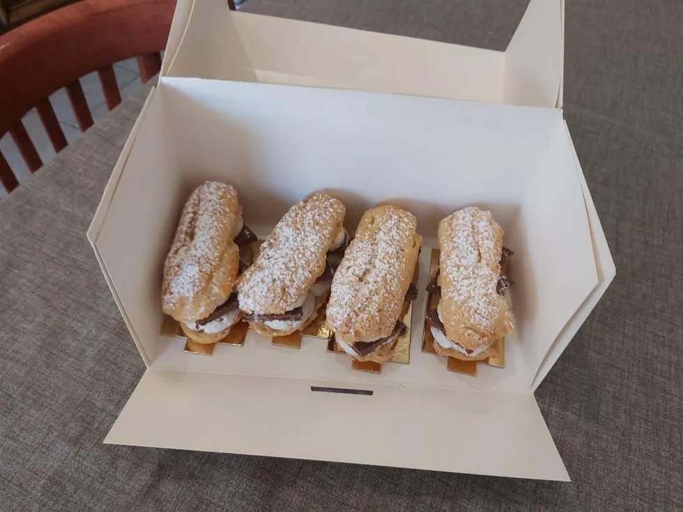 Quatre éclairs au chocolat saupoudrés de sucre glace dans une boîte pâtissière ouverte