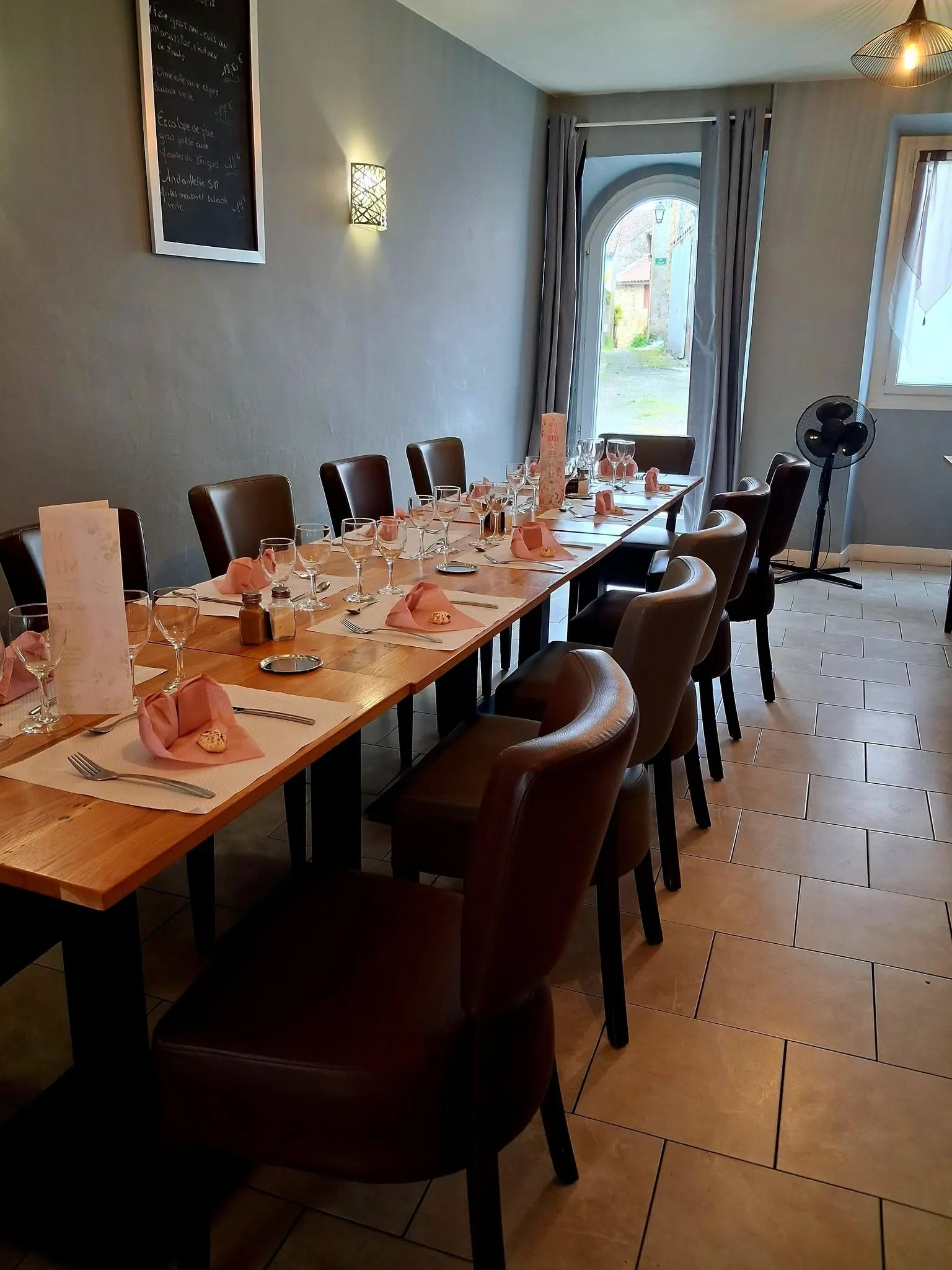 Longue table dressée avec serviettes corail et verres alignés dans la salle du restaurant