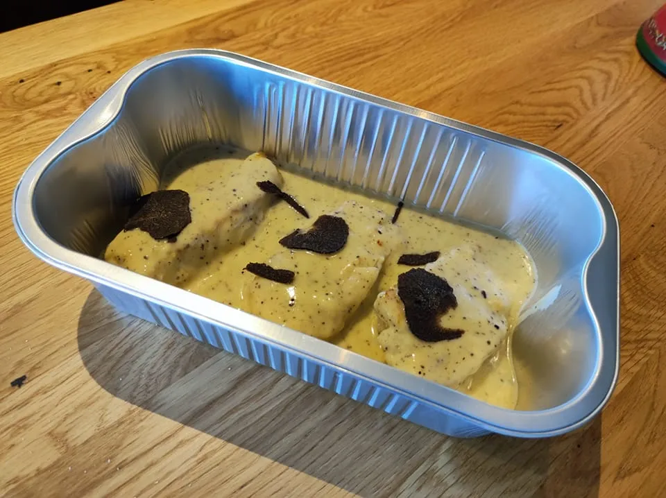 Plat en sauce crémeuse garni de lamelles de truffe dans une barquette à emporter