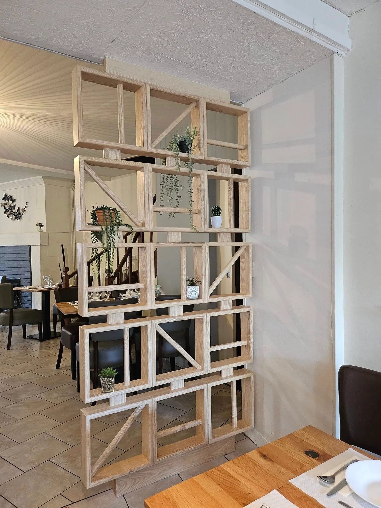 Salle de restaurant avec claustra en bois clair, plantes et tables dressées