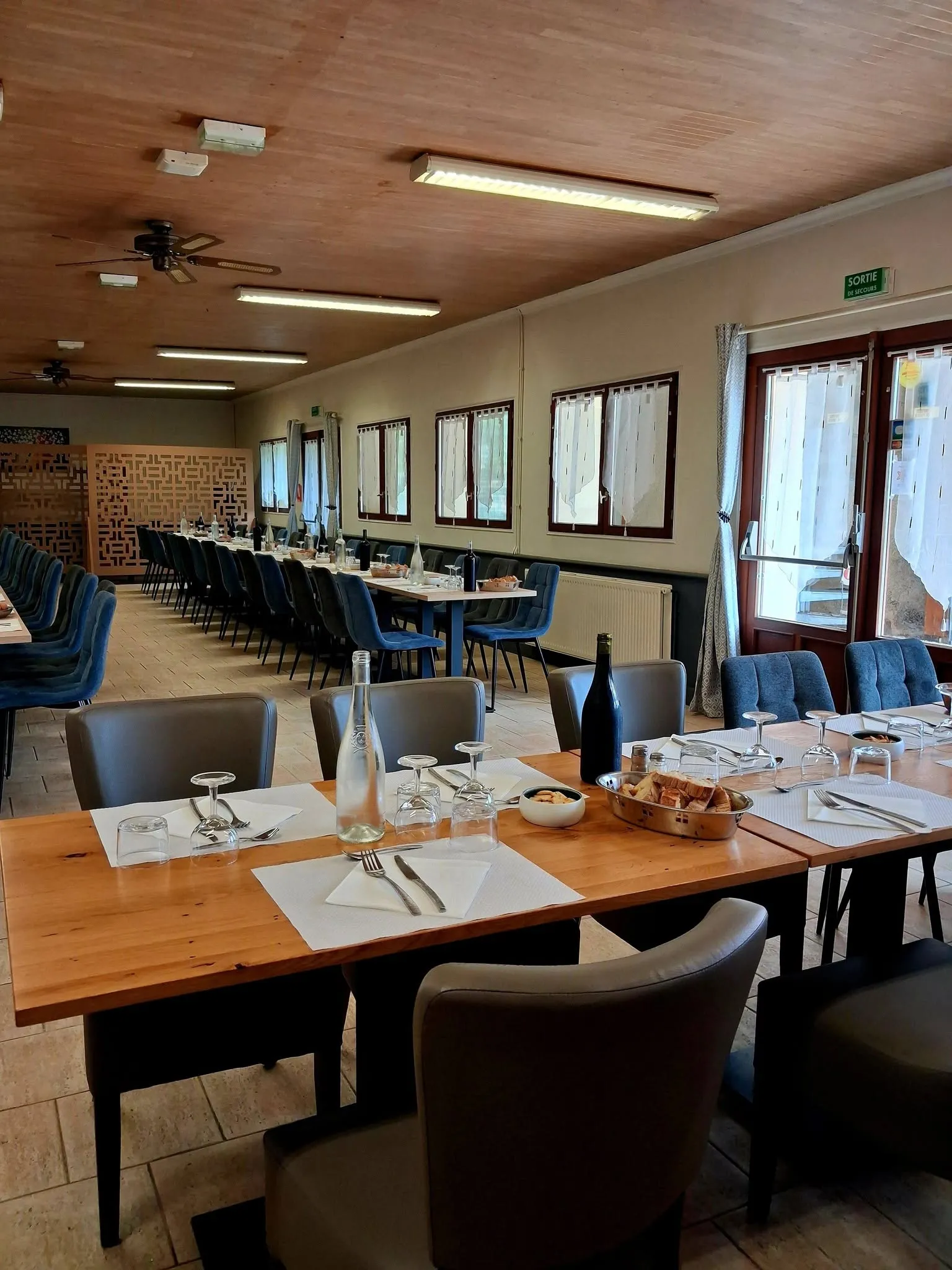 Salle intérieure du restaurant Le Corgnacois avec tables dressées et chaises bleues